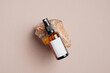 Amber glass spray bottle with white blank label on rock stone on beige background. Natural organic cosmetic product mockup. Flat lay, top view.