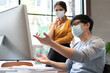 © eggeeggjiew - Young Asian Designers wear face mask work on computer monitor in office