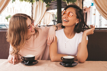 Two young beautiful smiling hipster girls in trendy summer casual clothes.Carefree women chatting in veranda terrace cafe and drinking coffee.Positive models having fun and communicating