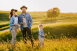 © iona - Happy family dressed in casual, enjoying holidays in nature during sunset with satisfied smiles. Parents wearing hats with a brim and holding glasses with white wine against hills on background.
