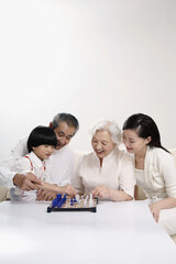 Wall Mural - Boy playing chess game with senior woman, woman and senior man watching