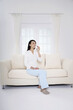© ImageHit - Woman sitting on the couch, drinking a glass of water
