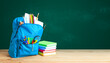 © adragan - School bag. Backpack with supplies for school on the background of green blackboard. Copy space for text.