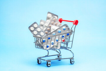 Wall Mural - Shopping trolley and medicine. Expensive medicine. Shopping basket with blisters with pills on a blue background