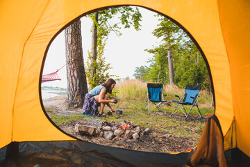 Wall Mural - view from camping tent woman cooking on burner near bonfire