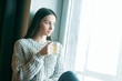 © VERSUSstudio - Beautiful woman drinking morning tea behind window