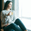 © VERSUSstudio - Beautiful woman drinking morning tea behind window