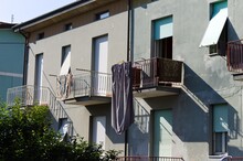 A Bed Sheet And Towels Hanging On A Drying Rack In The Balcony Of A House With White Shutters (Pesaro, Italy, Europe)
