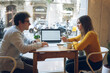 © makarovada - positive Caucasian freelancers work on a common design project connected to 4g wireless in coffee shop. using modern laptop with mockup screen. Concept of technology and online work.