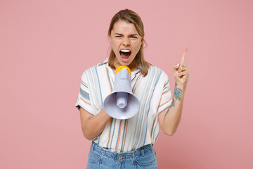 Wall Mural - Angry young blonde woman girl in casual striped shirt posing isolated on pastel pink background studio. People lifestyle concept. Mock up copy space. Screaming in megaphone, pointing index finger up.