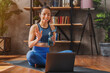 Young woman doing sports on mat with laptop online classes at home