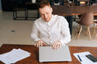 © dikushin - Professional young businessman wearing fashion casual clothing is closing on laptop lid at the table in modern office room. Concept of office working.