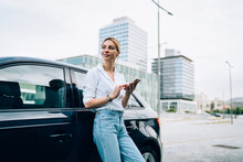 Stylish Woman With Smartphone Standing Beside Car And Looking Away