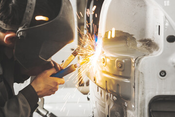 Worker in mask welds car in auto service of bodywork.