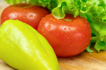 Beautiful, juicy vegetables with water drops Peppers, tomatoes, lettuce leaves on a wooden Board close-up