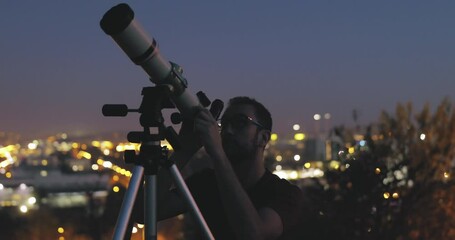 Wall Mural - astronomer with a telescope watching at the stars and moon with blurred city lights in the backgroun