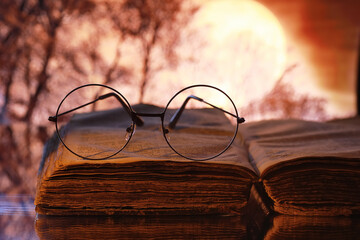 Wall Mural - Vintage glasses on an old retro book on a background of the moon. Reading a book by candlelight. The concept of book thrillers and novels.