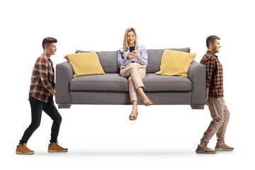 Two men carrying a sofa with a woman sitting on it and using a mobile phone
