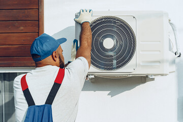 Wall Mural - Repairman in uniform installing the outside unit of air conditioner