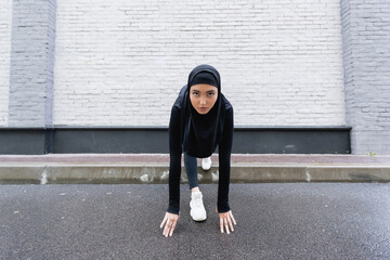 Young Muslim sportswoman in hijab and sportswear exercising near brick wall