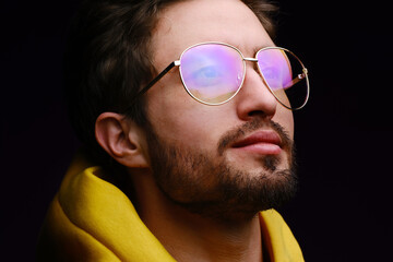 Wall Mural - A young man of 25-30 years in glasses and a yellow sweatshirt emotionally poses on a black background. 