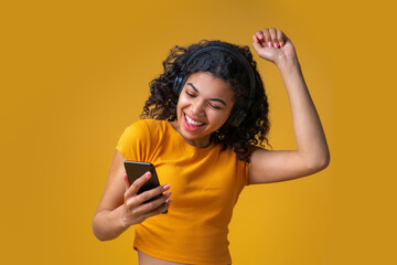 Wall Mural - Half length portrait of casually dressed cute girl chilling, enjoying listening to music via wireless headset, dancing over bright colored yellow background