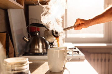 Morning coffee in the sun. Male hand pours freshly brewed coffee into cups.