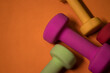 © OliaVesna - Bright pink, green, red and yellow small dumbbells on an orange background. Sport concept. High quality photo