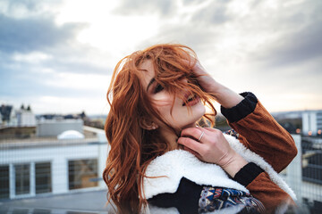 Wall Mural - Outdoor portrait of attractive sensual young woman. Millennial female model with face mostly covered with her beautiful long wavy red hairs.