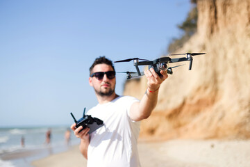 Young man holding drone before flight near ocean or sea. Pretty guy prepare to pilot outdoor