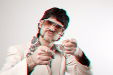 Retro Style Portrait Of A Retro Man In A 1970s Leisure Suit And Sunglasses Pointing To The Camera With A 3D Effect