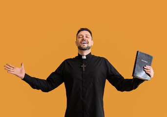 Wall Mural - Handsome priest with Bible on color background