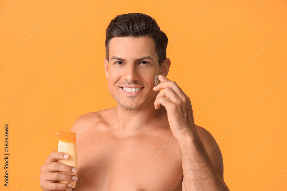Young man applying sunscreen cream against color background