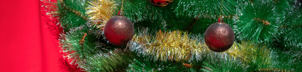 Christmas banner: two brown and gold Christmas balls weighs on a branch of a Christmas tree against a red background. The view from the top, place for text.