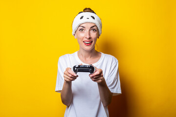 Poster - Young woman plays a virtual game with a joystick in her hands on a yellow background.