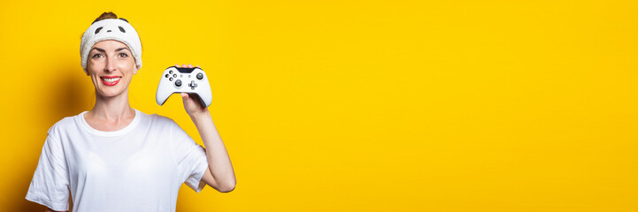 Young smiling woman holds a joystick in her hand on a yellow background. Banner