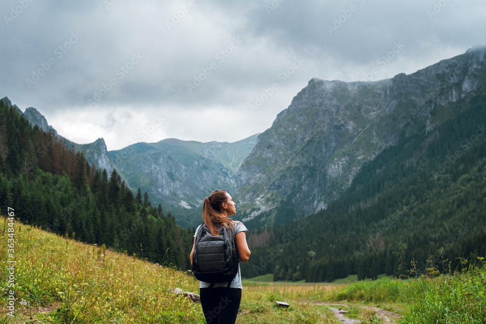 Rear shot of young brunette backpacker woman hiking on the green ...