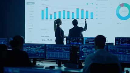 Wall Mural - Project Leader, Chief Executive Discuss Data Shown on Big Display. Screens Show Infographics, Charts, Finance Analysis, Stock Market, Growth.Telecommunications Control Room with Working Professionals