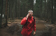 The terrified male traveler is talking on the phone, shouting in the mountain fir forest. A young tourist man in a red jacket with a backpack is feeling scared and lost in the woods.