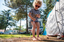 Cute Blonde Girl Helping Around Tent Pitch At Camping Resort.