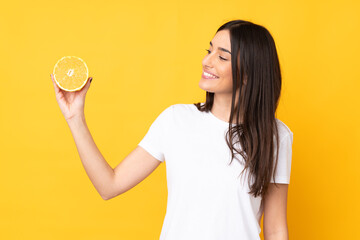 Wall Mural - Young caucasian woman holding an orange isolated on yellow background with happy expression