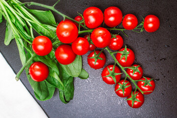 two ripe branches of cherry tomatoes and a white linen towel with spinach on a black embossed table. copy space, top view, flat lay, horizontal orientation