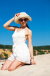 © Andrey_Arkusha - Young woman in sunglasses and a white dress posing against a blue sky