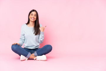 Wall Mural - Young caucasian woman isolated on pink background pointing to the side to present a product