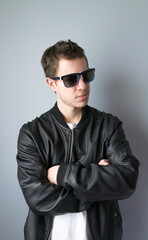 Modern young man in sunglasses and black jacket with arms crossed