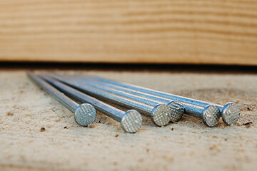 Fasteners and building materials for the roof. A pile of roofing long metal nails lying on pine for roof boards in close-up with a blurry background.