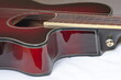 Der obere Teil von einer dunkel rote akustik Gitarre mit schwarz weißem Rand von der Seite fotografiert. Man sieht das runde Loch des Korpus, Teile des Griffbretts und der Seiten.