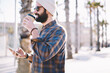 © BullRun - Trendy hipster guy drinking tasty coffee to go while walking down the street in sunny evening holding smartphone in hands. Caucasian male strolling outdoors with take away beverage enjoying weekend
