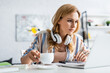 © LIGHTFIELD STUDIOS - Selective focus of pretty adult freelancer holding cup and working with laptop