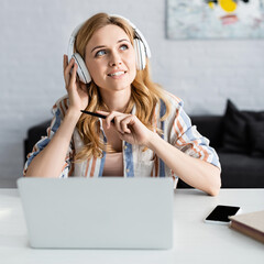 Selective focus of beautiful adult freelancer working with laptop and headphones